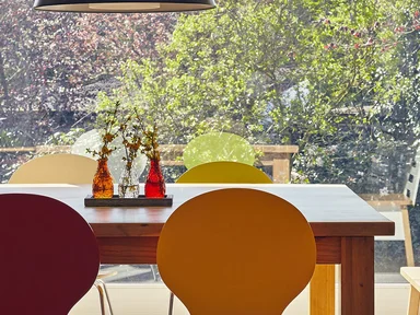 Tischgarnitur mit Holztisch und bunten Stühlen, Blick durch Fensterfront auf Garten